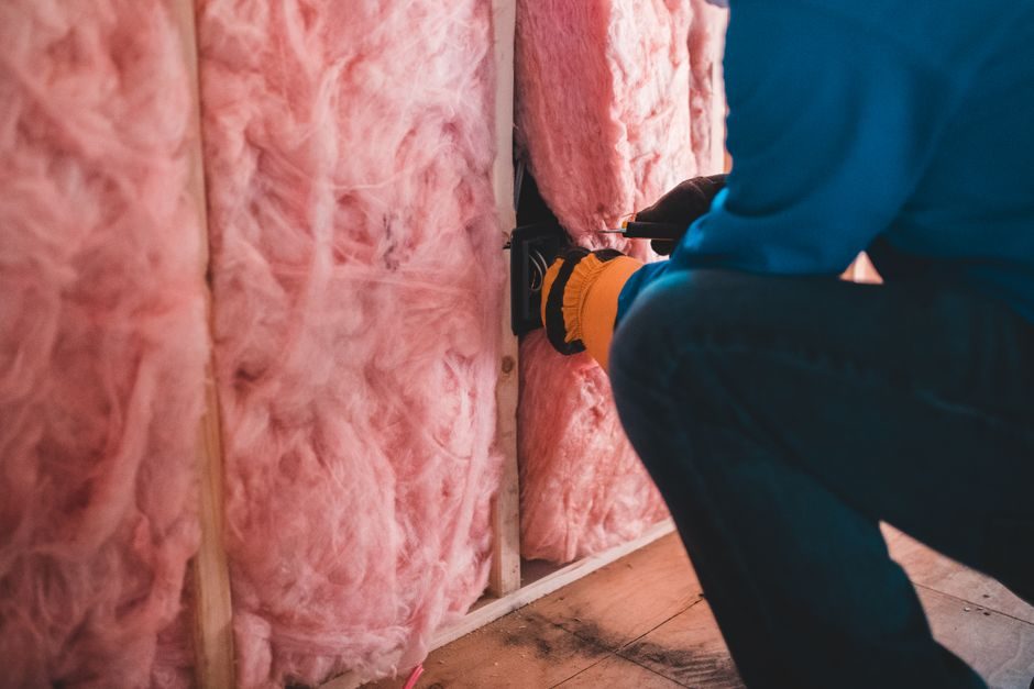 Crop unrecognizable worker in gloves sitting on haunches and insulating with pink stone wool
